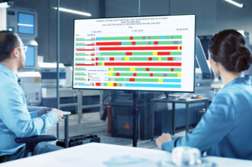 Dos ingenieros de equipos en una sala de conferencias de una fábrica mirando un diagrama de Gantt de FabTime Tool State en un monitor.